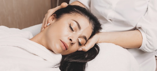 Head massage procedure with a brunette caucasian lady lying on the couch at the spa salon