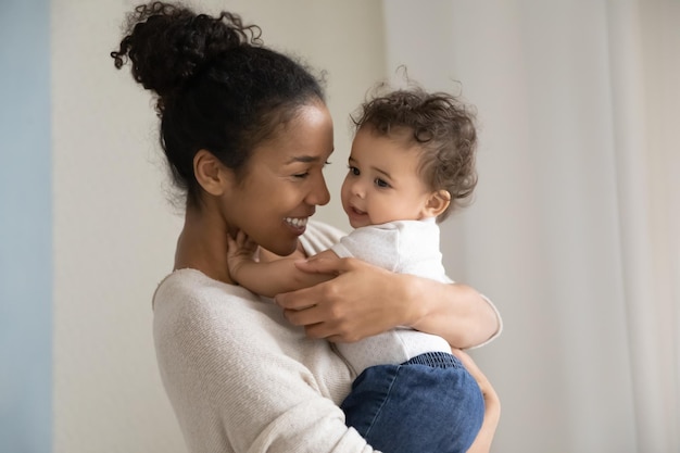head shot affectionate millennial biracial mommy or babysitter carrying on hands funny cute curly mixed race kid girl or boy enjoying daycare time together indoors responsible parenting concept