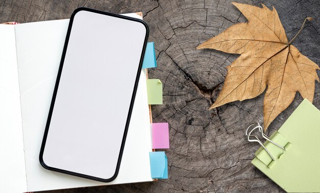 Photo over head shot of blank screen smartphone and notebook on wooden background.