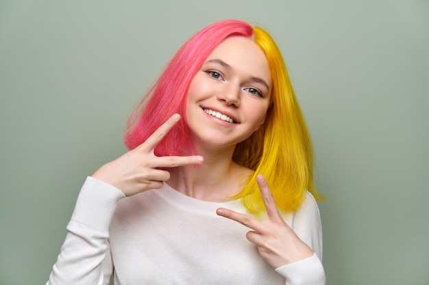 녹색 배경에 트렌디한 염색 머리를 한 여성의 손가락으로 승리 제스처를 보여주는 세련된 아름다운 10대 소녀의 헤드 샷 십대 16 17세 청소년 감정 라이프 스타일