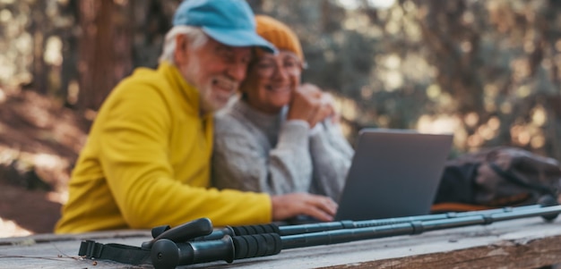 Портрет с головой вблизи милой пары пожилых людей среднего возраста, использующих компьютер на открытом воздухе, сидящих за деревянным столом в лесу горы в природе с деревьями вокруг них