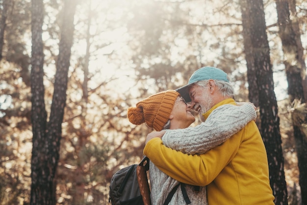 Head shot portrait close up of old people smiling and enjoying looking each other in the forest of mountain Cute couple of mature seniors in love feeling happy and taking care Sun at the background