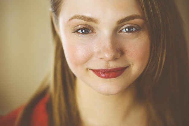 Head shot of a smart confident smiling millennial european woman standing with folded arms at home. Attractive young  teenager student girl freelancer looking at camera, dressed in red.