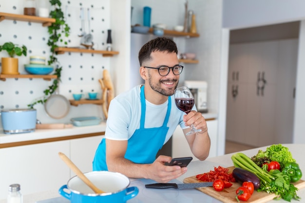 自宅でベジタリアン ディナーの食事を準備しながら、ソーシャル ネットワークでスマート フォン チャットを使用して笑顔の若い男