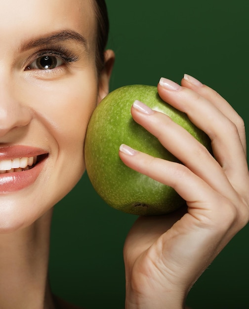 Head shot of woman holding green apple against green background