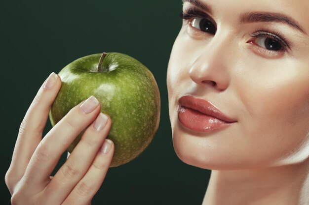 Head shot of woman holding green apple against green background