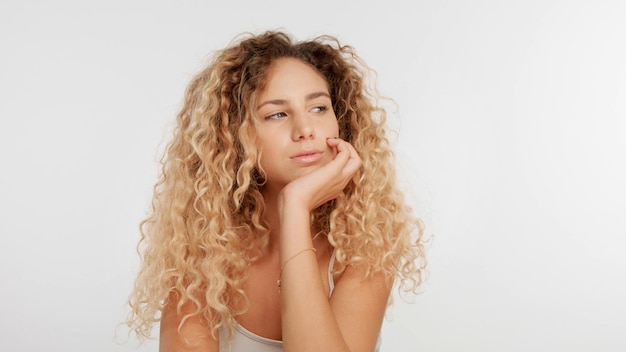 Head and shoulders plan of blonde wooman with big curly hair in studio on white Bored woman