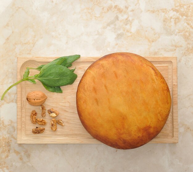 Head of smoked Suluguni cheese on wooden board with walnuts and basil