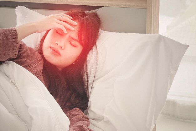 Mal di testa da febbre. la donna asiatica ha mal di testa e influenza su un letto bianco.