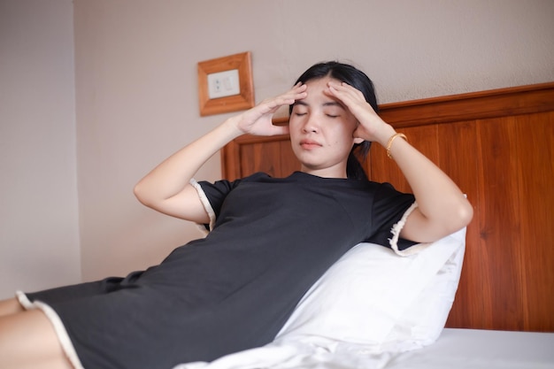 Headache woman Closeup photo of a beautiful woman who is sitting on a bed in bedroom with her eyes closed touching her head while suffering from a migraine