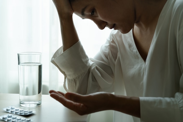 La mano delle donne di emicrania tiene la medicina con un bicchiere d'acqua