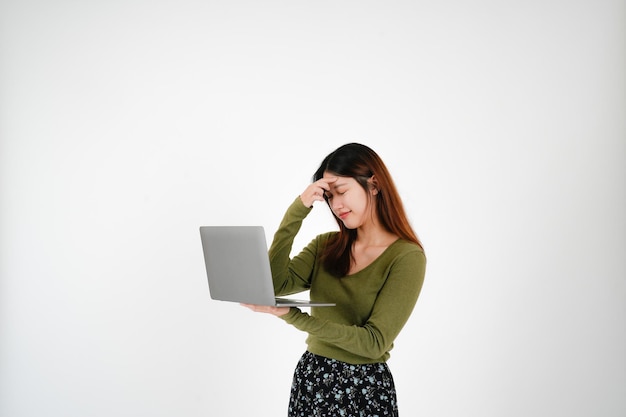 두통이 있는 젊은 아시아 여성이 흰색 스튜디오 배경에서 노트북 컴퓨터를 들고 진지하게 포즈를 취하고 있습니다.