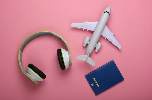 Headphones, airplane figurine, passport on a pink pastel surface