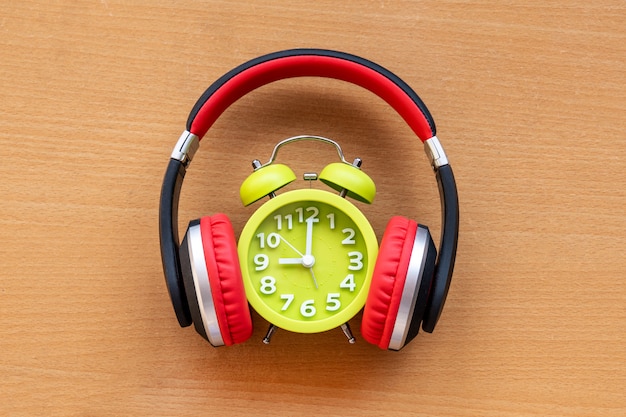 Headphones and alarm clock on wooden desk. Musical concept