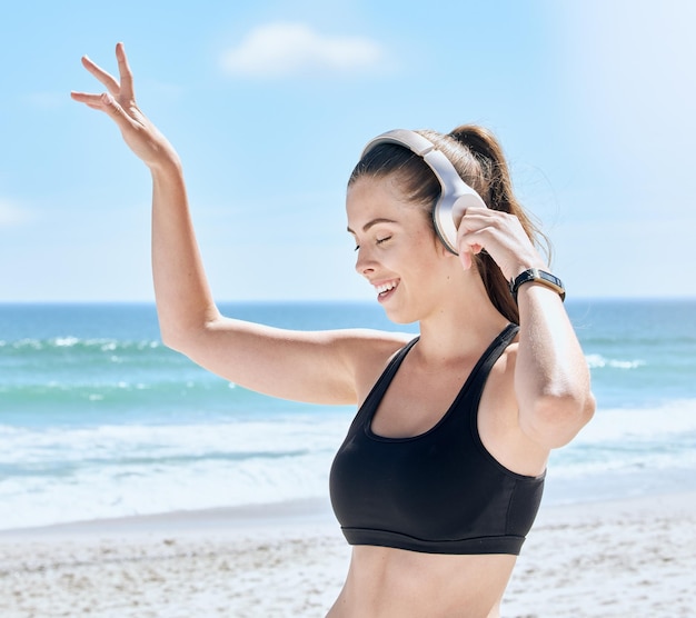 Headphones beach and woman dance after workout training or exercise Freedom energy and happy fitness female streaming audio podcast or radio music at sandy seashore or ocean coast outdoors