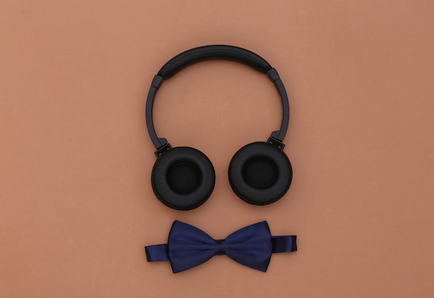 Headphones and bow tie on brown background. Top view