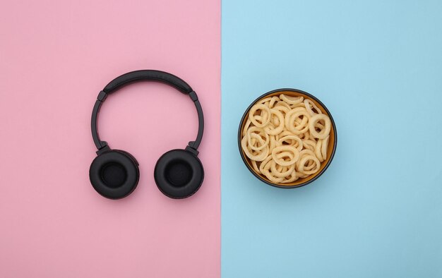 Headphones and a bowl of corn rings on a blue-pink pastel background. Top view