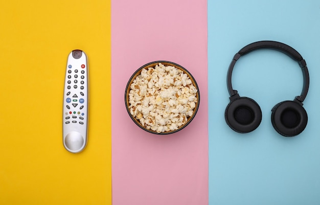 Headphones and bowl with popcorn, tv remote on colored pastel background. Top view. Flat lay