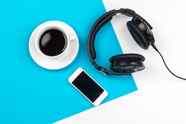 Headphones and coffee cup on blue background, top view