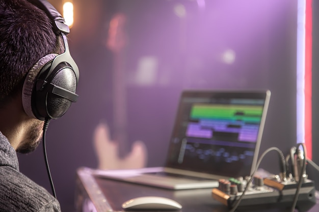スタジオライト付きの音楽スタジオのミュージックミキサーとラップトップに接続されたヘッドフォンをクローズアップします。