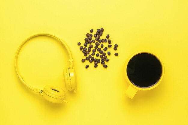 Headphones, a cup of coffee and coffee beans on a yellow background. Morning accessories.