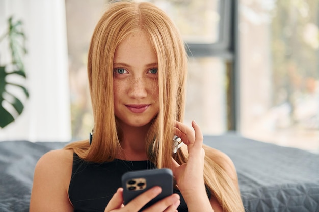 헤드폰에 금발 머리카락을 가진 십대 여성이 낮에는 집에 있습니다.