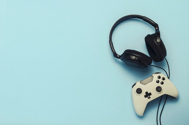 Headphones and gamepad on a blue background. . Concept of computer games, entertainment, gaming, leisure. Flat lay, top view