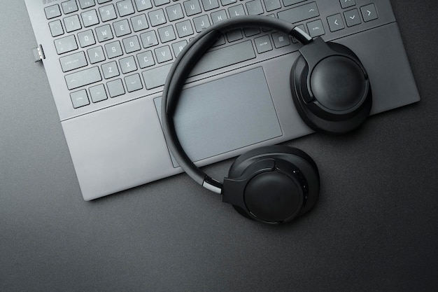 Headphones and laptop computer on black desktop Listening to music audio sound concept