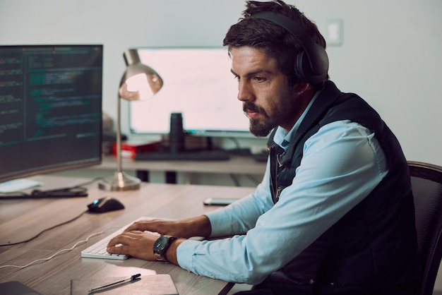 Headphones programmer and man typing on computer coding or programming at night Information technology thinking and male developer or coder working on software while streaming music or podcast