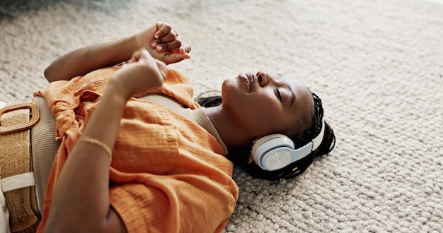 Photo headphones relax and young woman on the floor in the living room listening to music or radio at modern apartment dancing smile and young african female person streaming song in the lounge at home