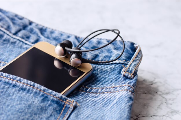 Headphones and smartphone in the pocket of jeans, close-up