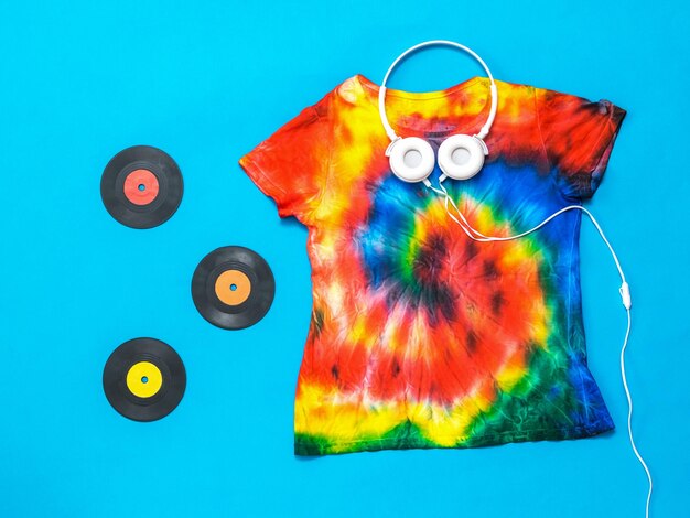 Headphones vinyl discs and a tie dye tshirt on a blue background Flat lay Pastel color