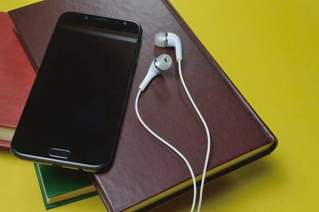 Headphones with books and a smartphone on a yellow background.