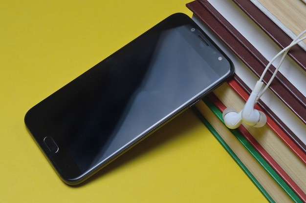 Headphones with books and a smartphone on a yellow background.