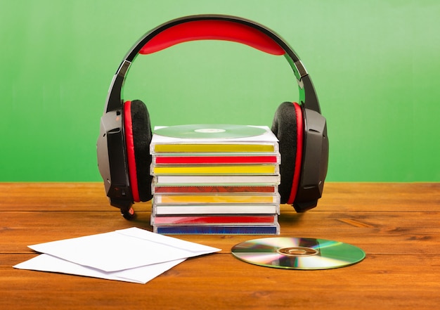 Photo headphones with cds on a wooden table, on a green wall.