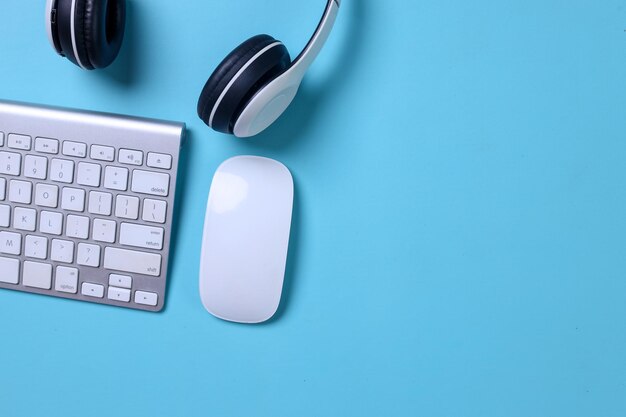 Headphones with computer keyboard and mouse on blue background Top view Space for text