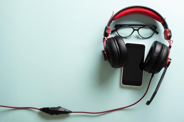 Headphones with glasses and a smartphone on a light blue background The desktop of a modern blogger with a place for text