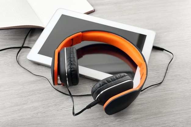 Headphones with tablet and notebook on wooden table close up