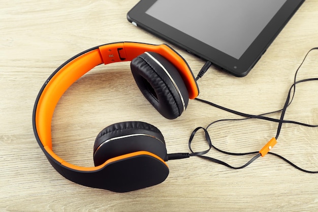 Headphones with tablet on wooden table close up