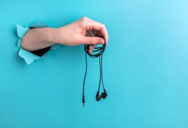 Headphones in a woman's hand on a blue background with a hole