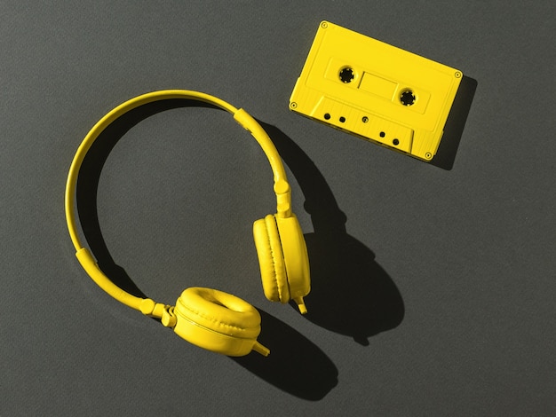 Headphones and a yellow cassette with a magnetic tape on a black background in bright light. Color trend. Flat lay.