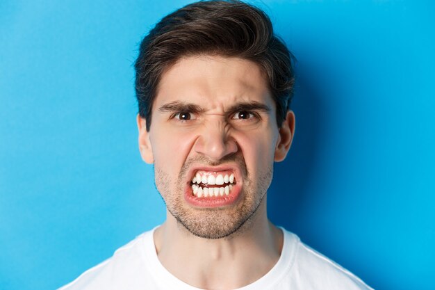 Photo headshot of angry caucasian man looking with scorn and dismay, being mad at person, standing against blue background.