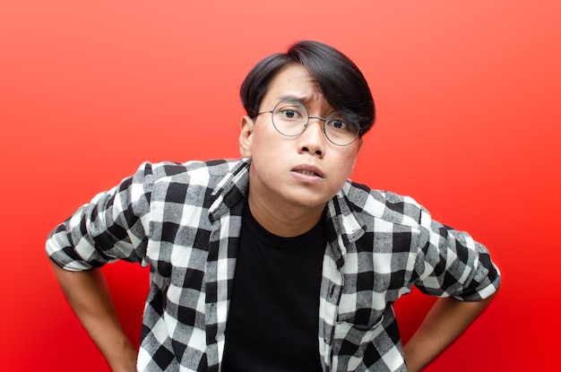 Headshot of asian young man having doubt with unsure\
expression. man raising eye brow to intimidate.