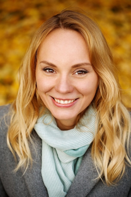 Foto colpo in testa di una bella donna con i capelli lunghi biondi e un bel sorriso e gli occhi marroni in autunno