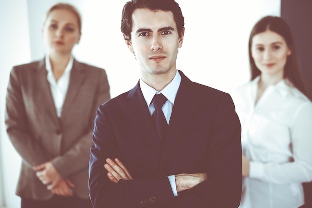 Headshot of businessman standing straight with colleagues at background in office. Group of business people discussing questions at conference or presentation. Success and business concept.