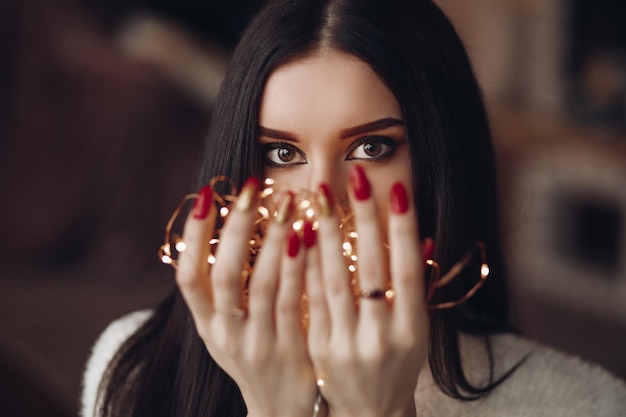 Photo headshot of darkhaired woman with bright evening make up holding bunch of lights in her hands with red nails