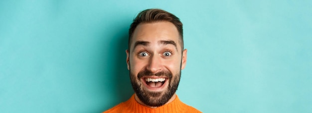 Headshot of handsome caucasian man with beard smiling happy at camera staring amazed standing in ora