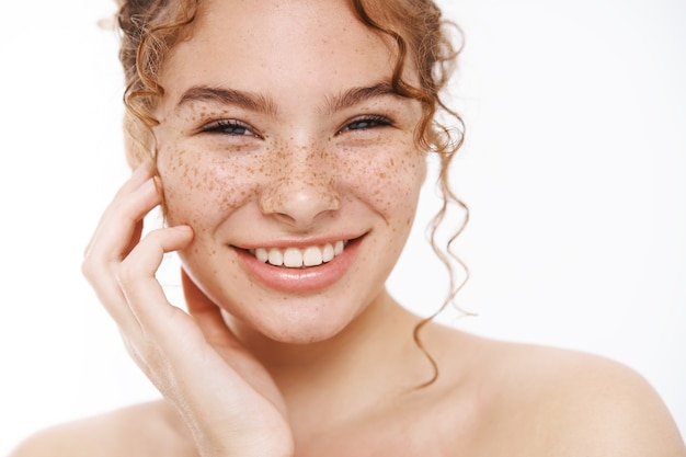 Headshot happy tender redhead girl freckles smiling broadly white teeth standing naked gently touching cheek taking care body showering, applying skincare cosmetics treatment, daily hygiene procedure