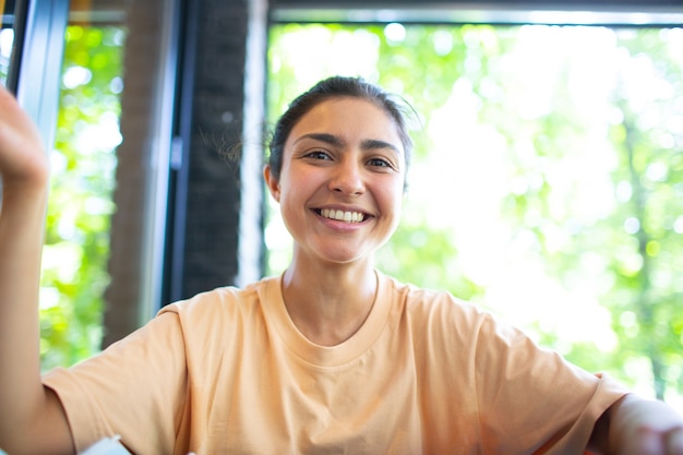 Headshot of indian woman sit on potdoor cafe waving hand looks to camera make video call chat use co...