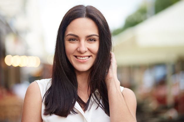 Headshot of pleased brunette female looks happily at camera